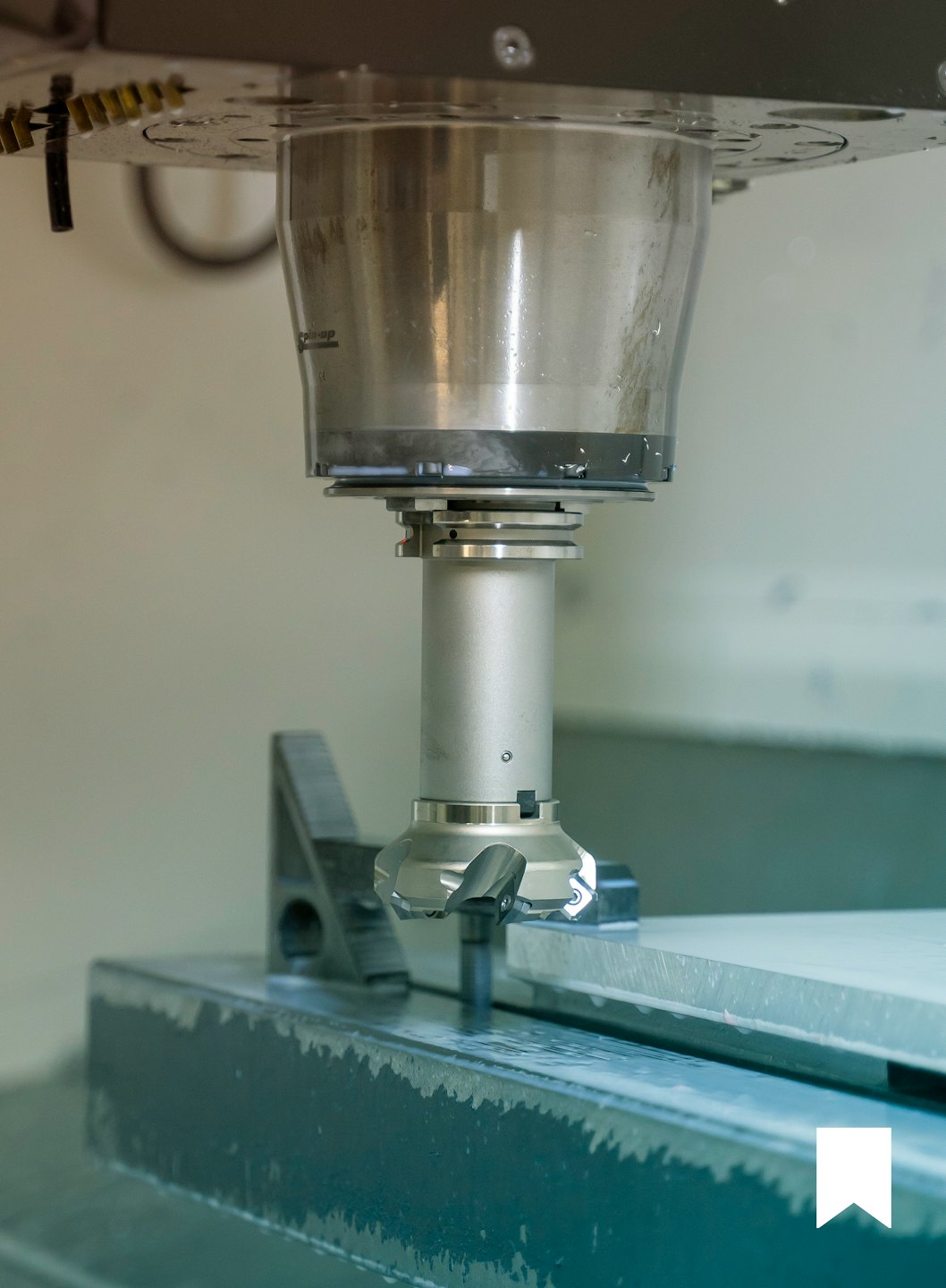 Fresatrice CNC che lavora un pezzo metallico con refrigerante.