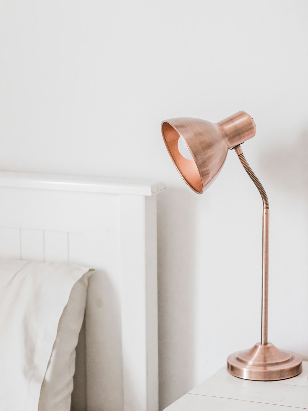 Lampada da scrivania color oro rosa su un comodino bianco.