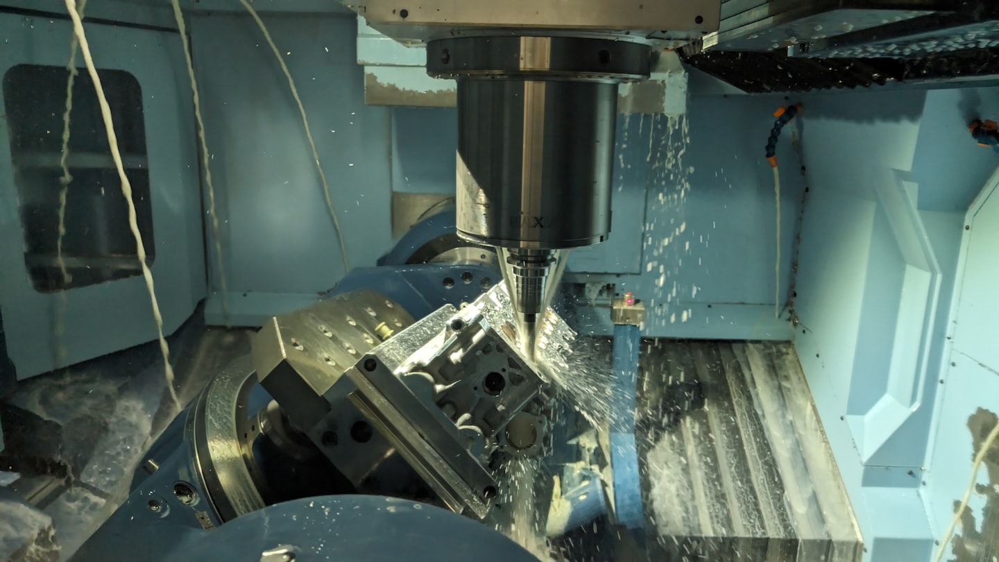 Fresatrice CNC spruzza liquido refrigerante su un pezzo di metallo.